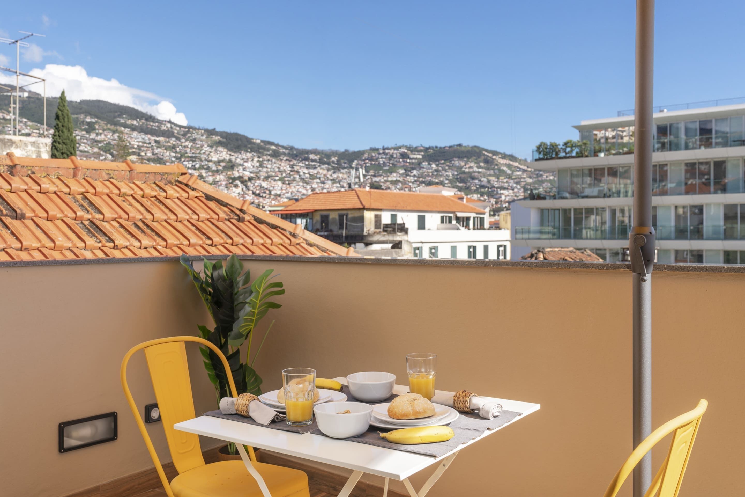 A balcony with a table set for breakfast, including plates, bowls, and a banana.