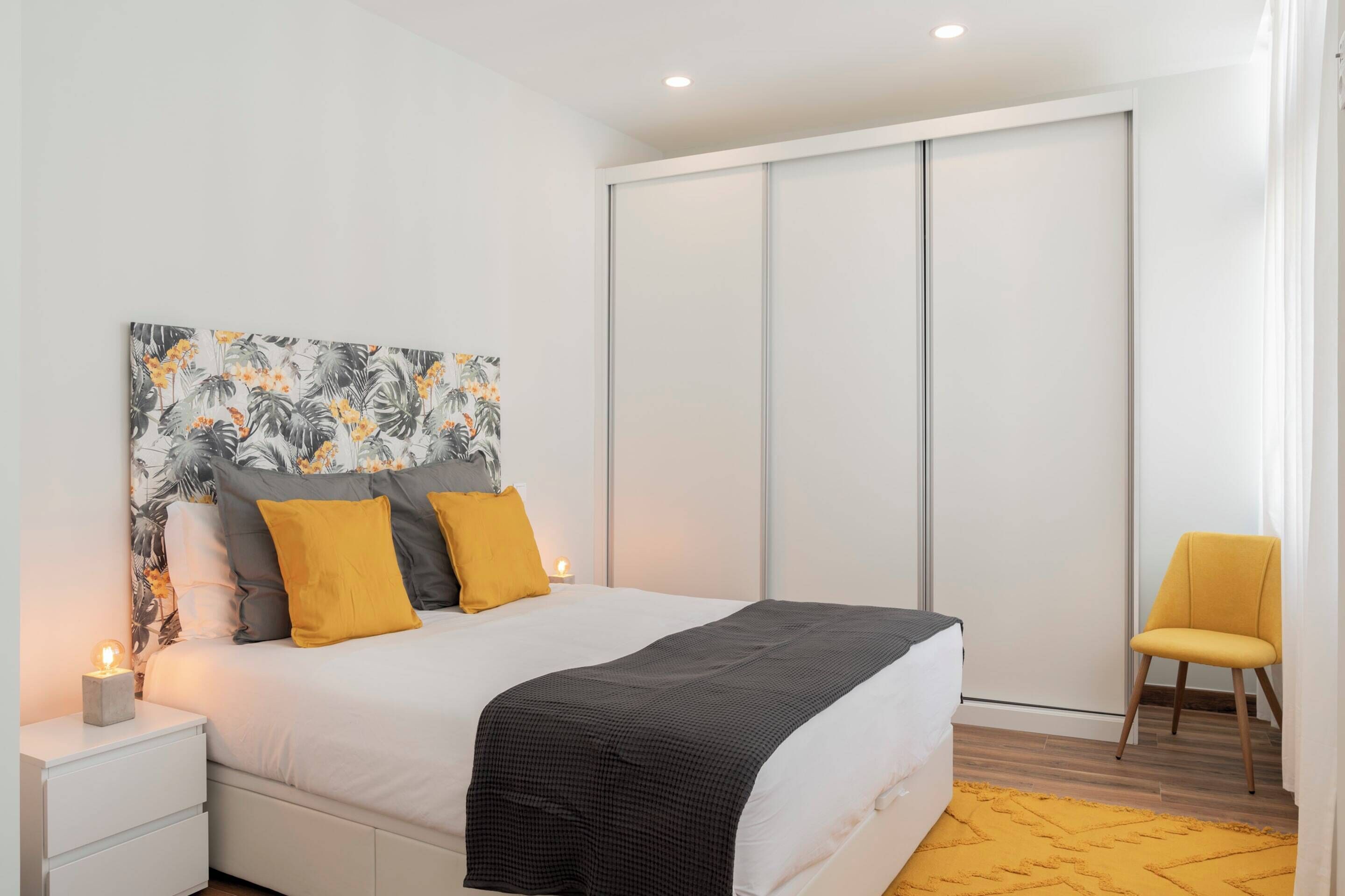 A modern bedroom with a bed, a nightstand, a chair, and a sliding door closet.