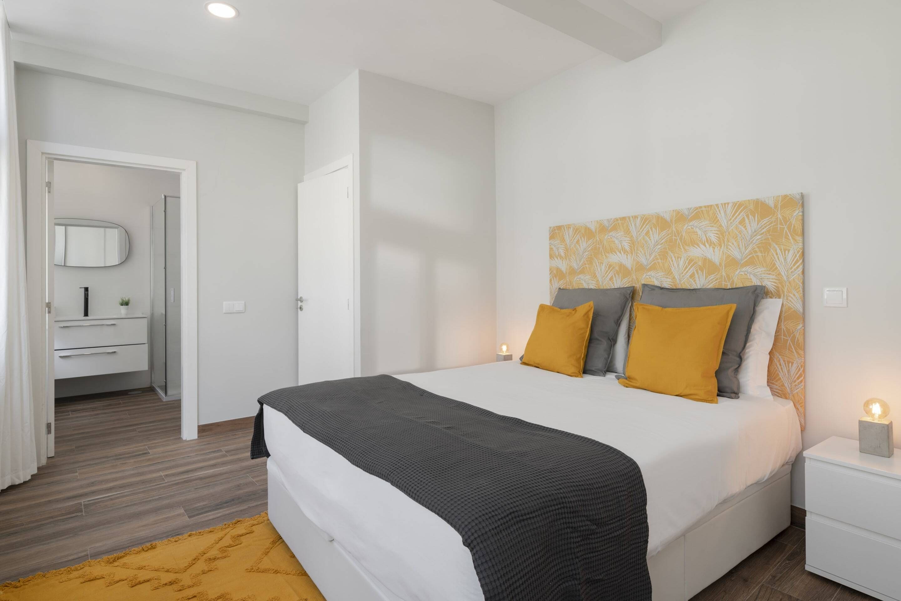 A modern bedroom with a large bed, a nightstand, a bedside lamp, and a mirror.