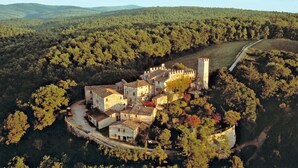 An aerial view of a historic stone castle surrounded by dense forest, with a winding road leading to it. - Castello di Montalto - San Martino (Castelnuovo Berardenga)