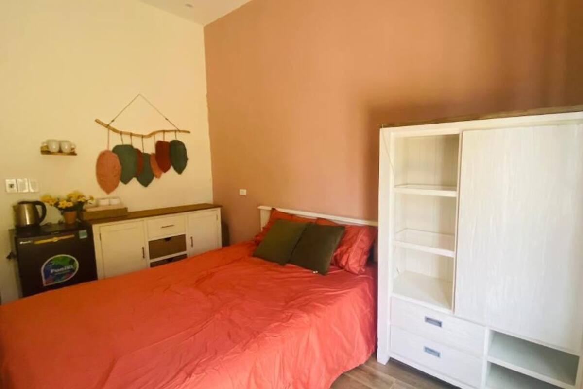 A bedroom with a bed, a wardrobe, a small table with a kettle, and a wall-mounted drying rack.