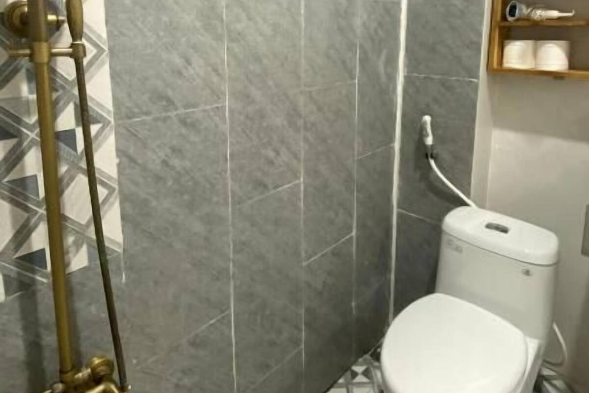 A bathroom with a shower, toilet, and a shelf with toiletries.