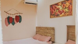 Habitación de hotel con dos camas, cabecero de madera, aire acondicionado montado en la pared y un cuadro con motivos florales.