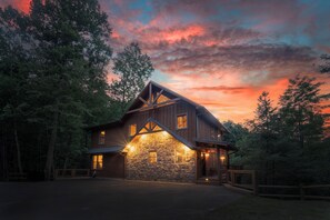 A rustic cabin with a stone facade, wooden beams, and a porch with lights.