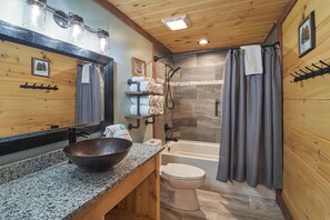 A wooden cabin bathroom with a granite countertop, a white toilet, a bathtub, and a shower curtain.