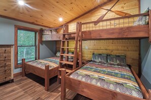 A bunk bed room with a ladder, wooden walls, a window with blinds, and a dresser.