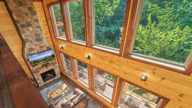 A high-ceilinged room with a stone fireplace, large windows, and a view of the outdoors.
