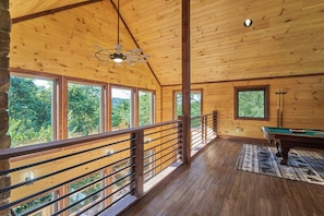 A wooden interior with a pool table, large windows, and a balcony.