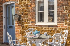 A stone building with a blue door labeled "Sea View Outie," white ornate chairs, a table with a blue teapot, and a window with a view. - Seaview Cottage, Old Hunstanton, Norfolk (Old Hunstanton)