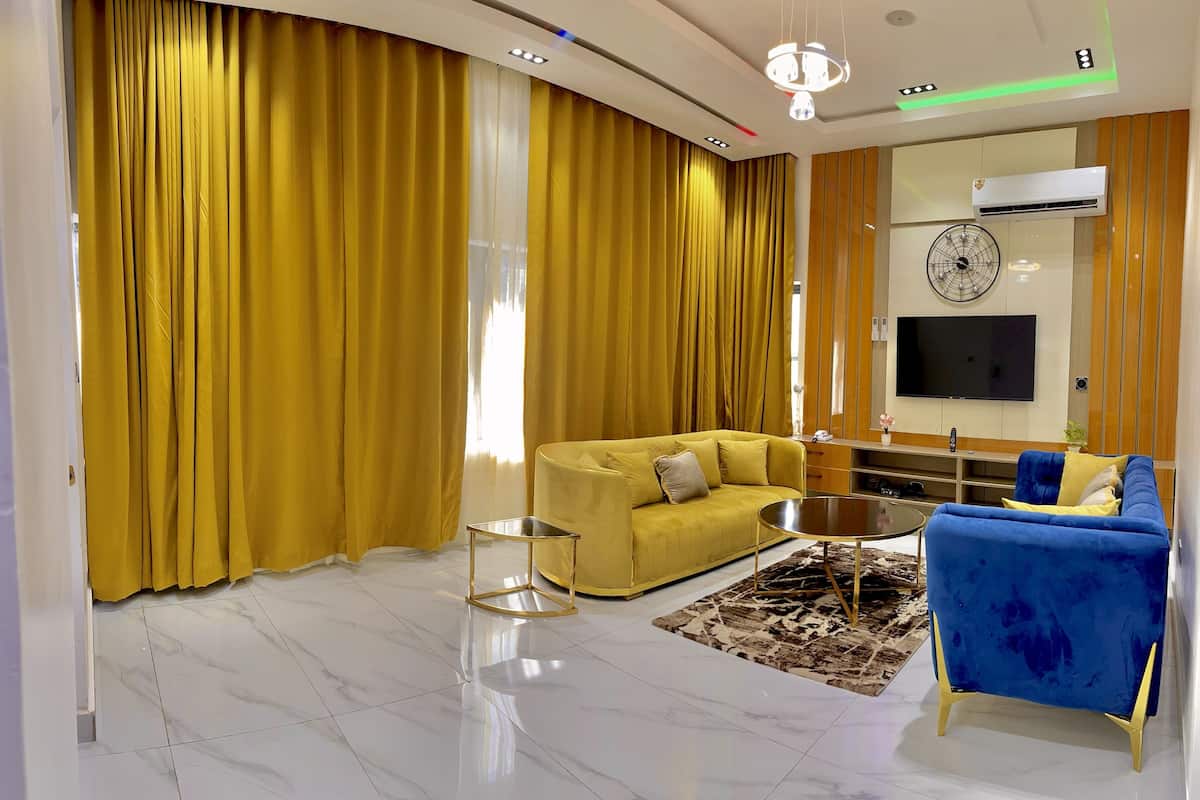 Un salon moderne avec un canapé jaune, un fauteuil bleu, une table basse et un téléviseur fixé au mur.