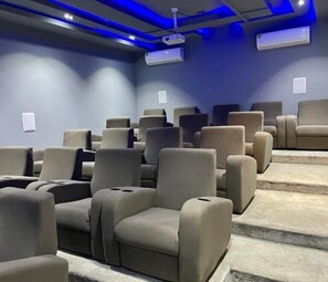 A movie theater with rows of beige seats, a blue-lit ceiling, and air conditioning units on the walls. - Lisa Suites (Abuja)