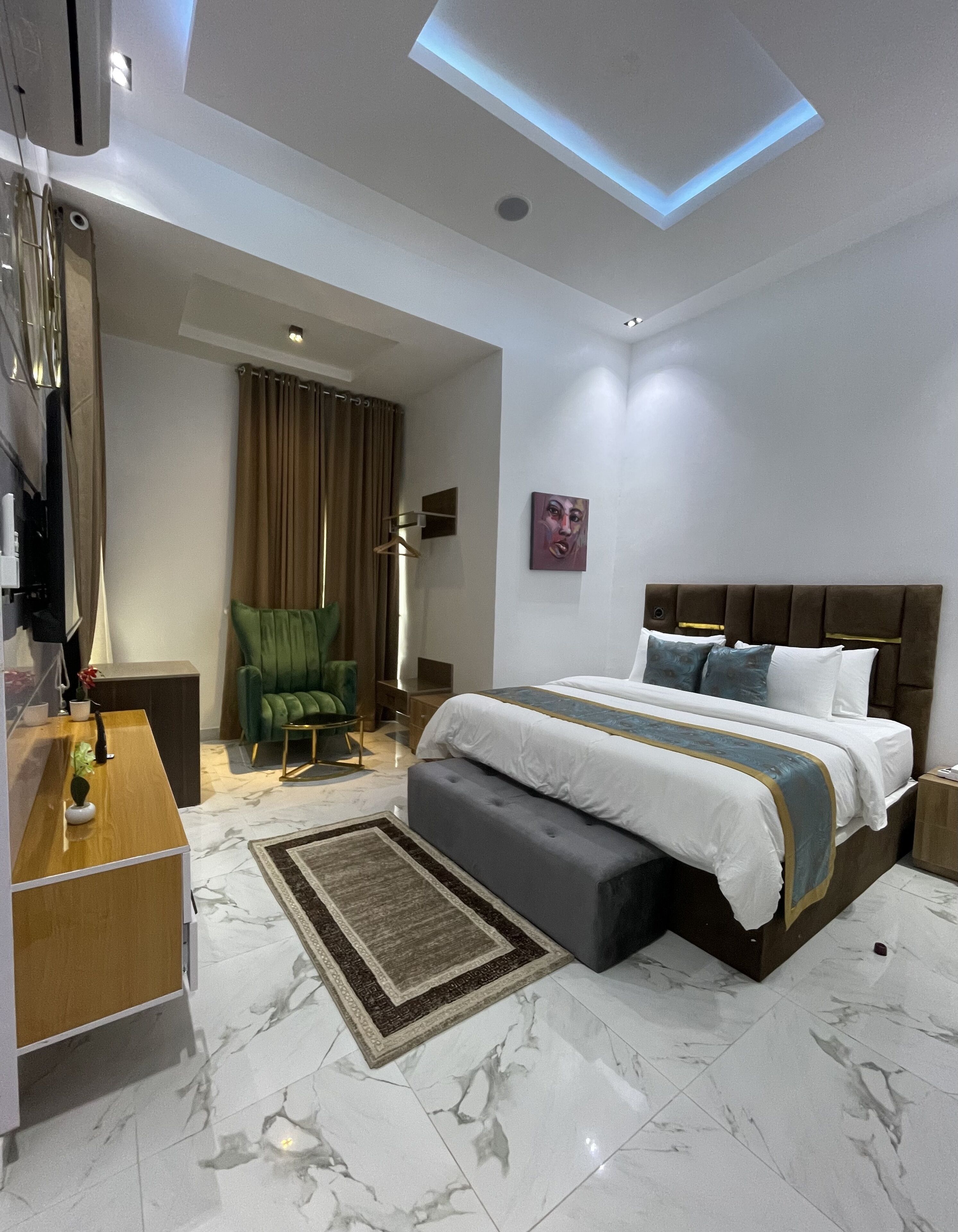 A modern hotel room with a large bed, a desk, a chair, and a floor lamp.