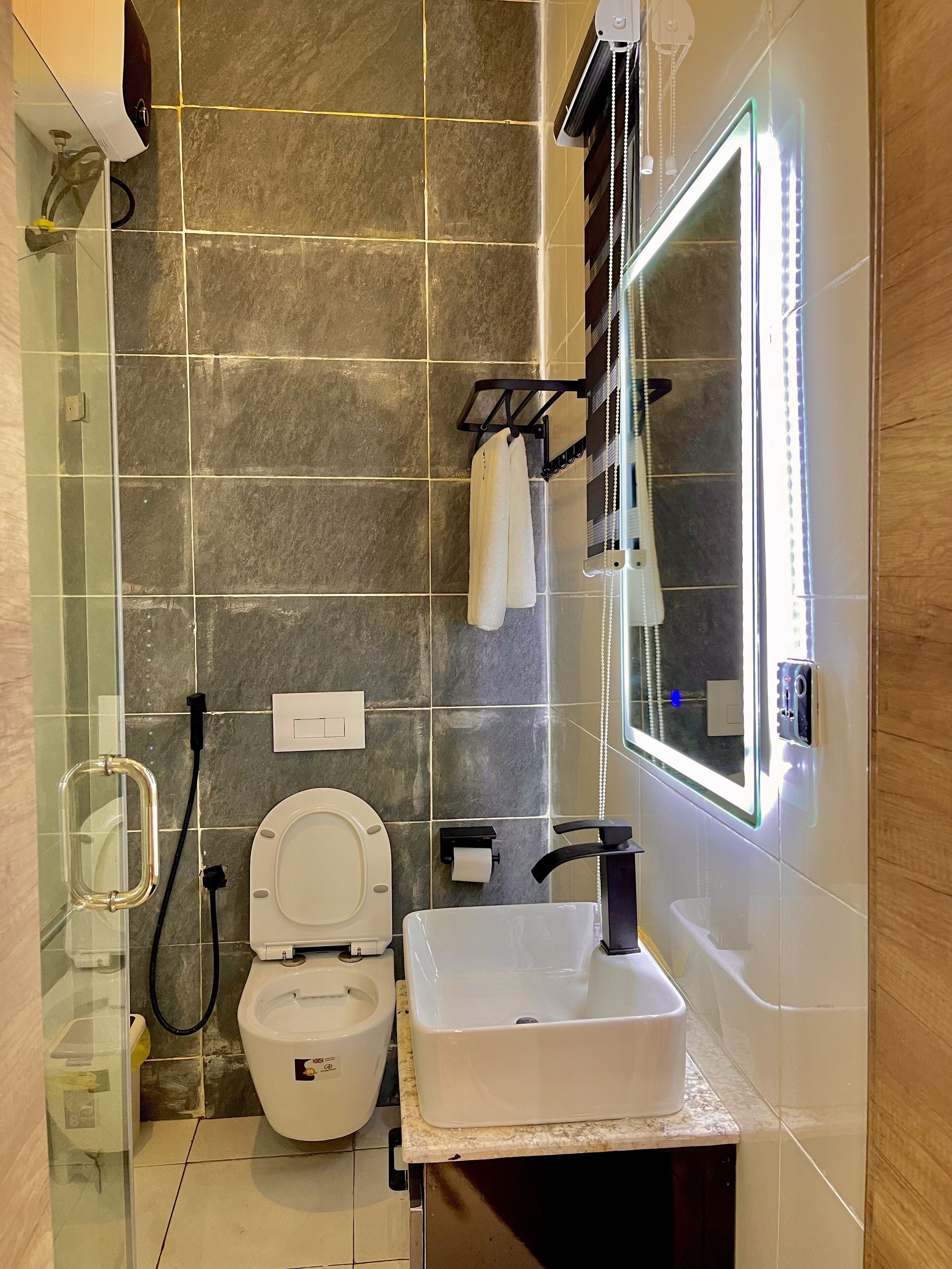 A modern bathroom with a glass shower enclosure, a toilet, a sink, and a mirror with LED lights.