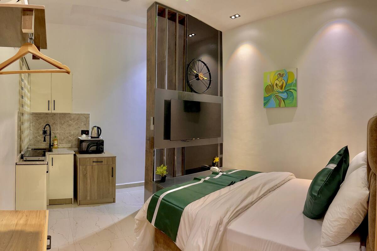 Une chambre moderne équipée d’un lit, d’une télévision, d’une horloge et d’une kitchenette.