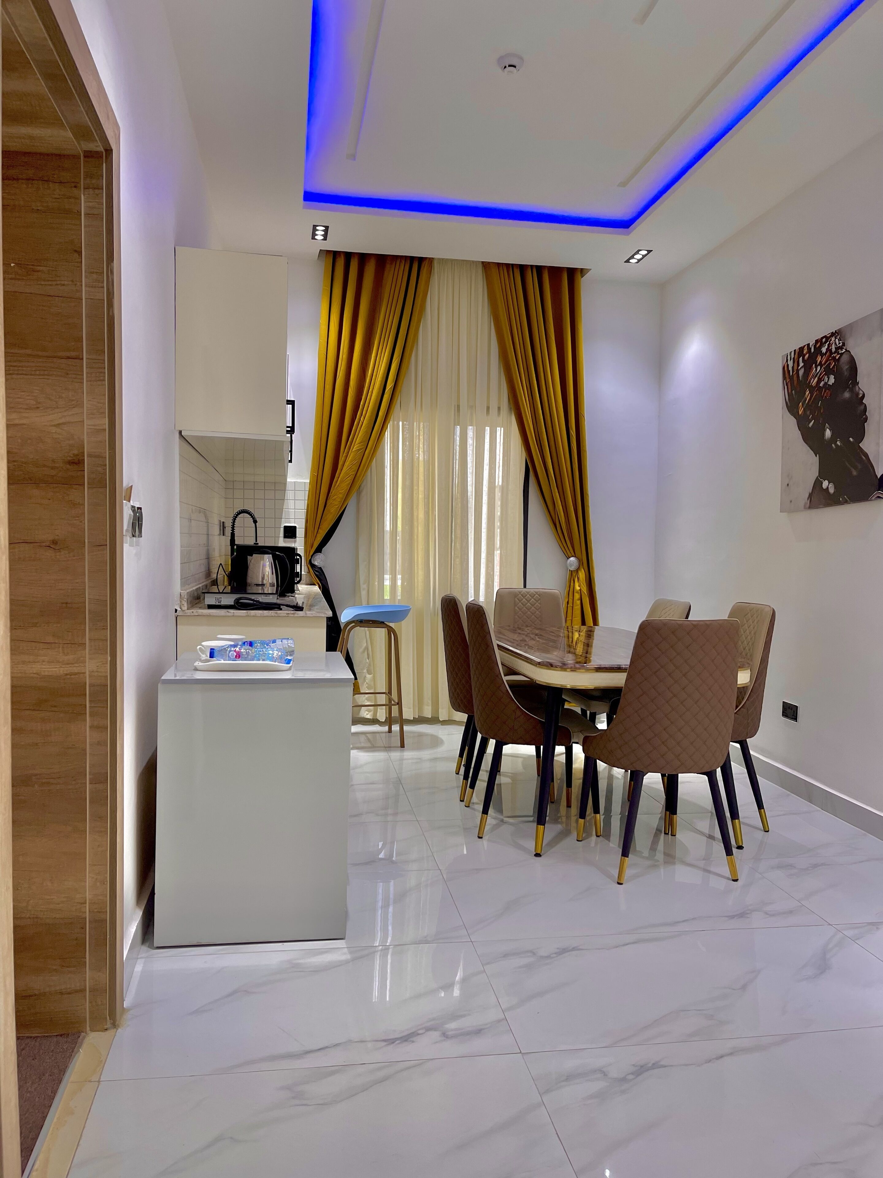 A modern dining area with a marble floor, a central island with a kettle, and a dining table with chairs.
