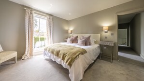 A bedroom with a large bed, two bedside tables, a bench, and a window with curtains. - Old Mill House, Brancaster, Norfolk (Brancaster)