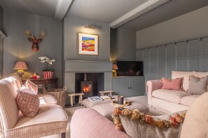 Un salon chaleureux avec une cheminée, une tête de cerf accrochée au mur et un tableau représentant un paysage, encadré.