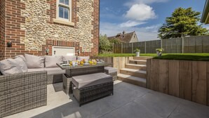 A patio area with wicker furniture and a stone wall. - Old Mill House, Brancaster, Norfolk (Brancaster)
