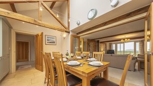 A dining area with a wooden table set for six, surrounded by wooden chairs with leather cushions. A stone wall and a stone fireplace are visible in the background. - 6 Courtyard Barn, Docking, Norfolk (Docking)