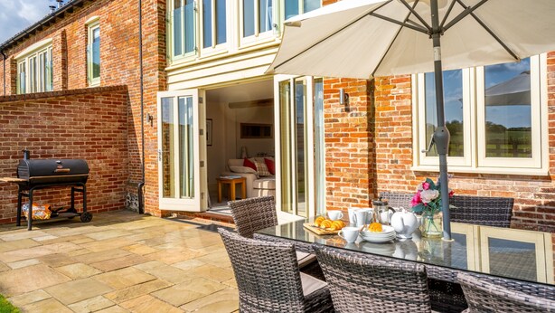 A patio with a glass table, wicker chairs, and a barbecue grill. - 6 Courtyard Barn, Docking, Norfolk (Docking)
