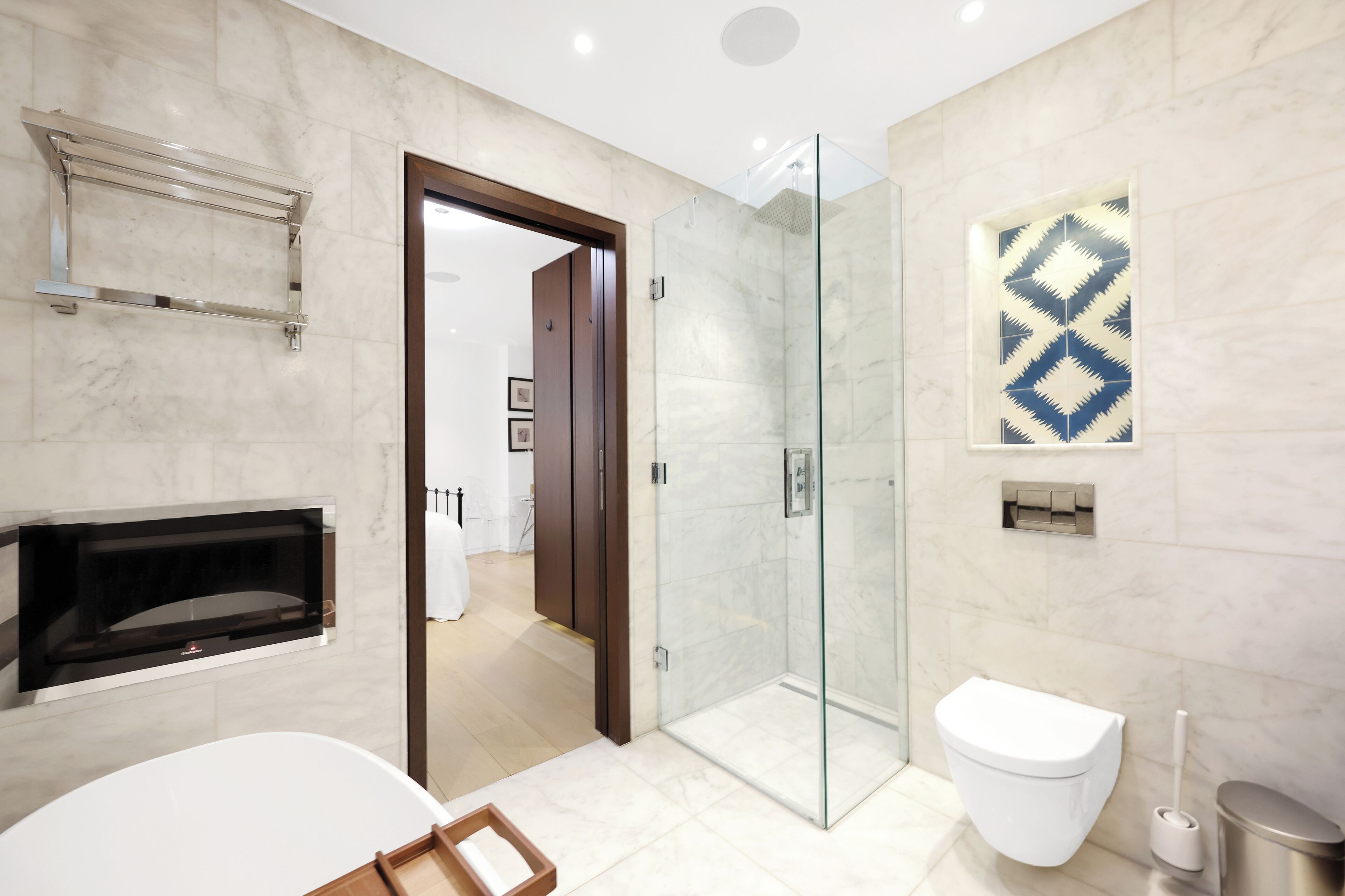 Une salle de bain moderne avec une douche à parois de verre, des toilettes blanches, un lavabo intégré et un mur recouvert de carreaux de marbre.