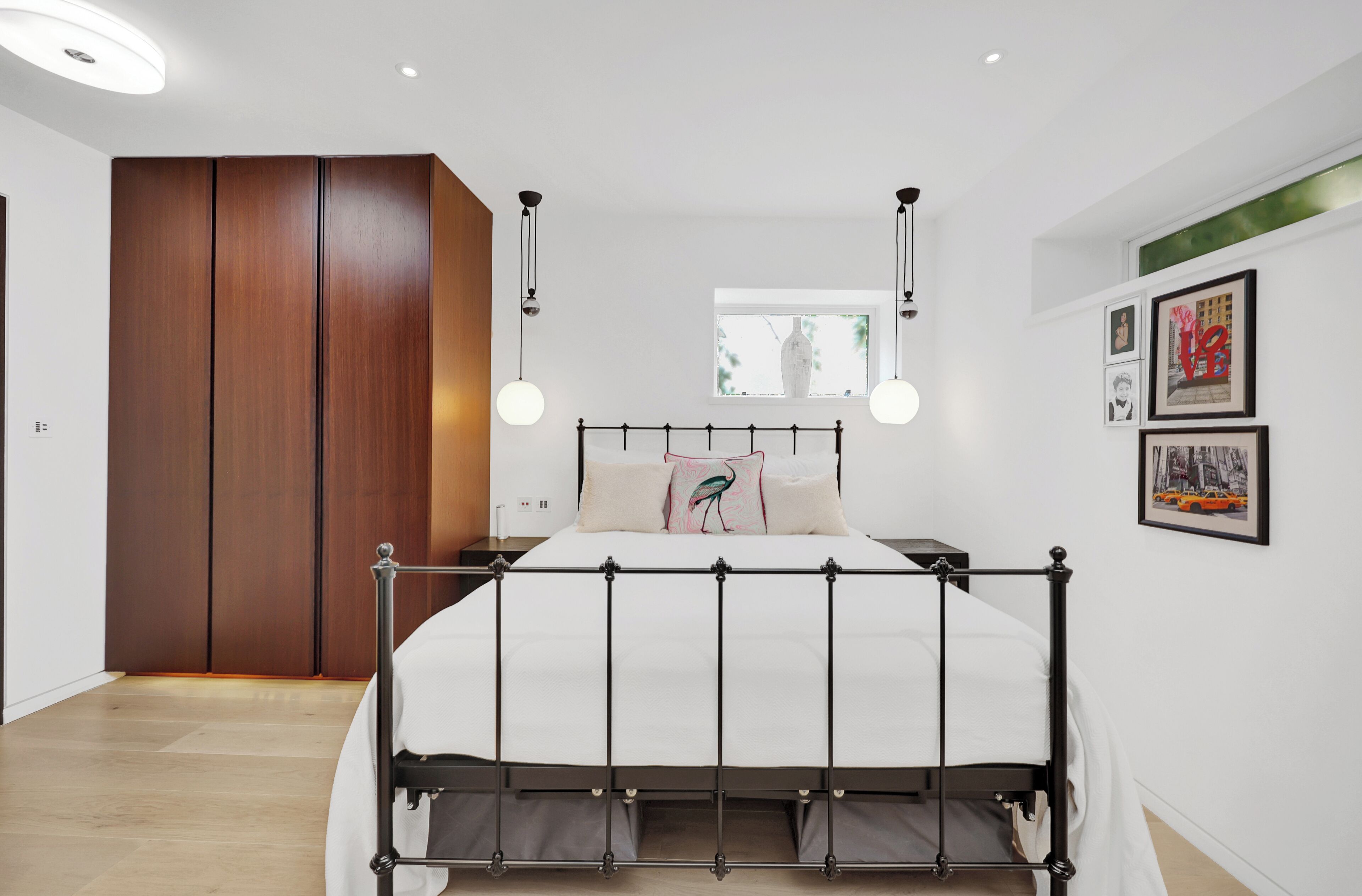 A modern bedroom with a metal bed frame, a wooden wardrobe, and a window with a view of greenery.