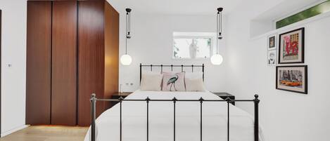 A modern bedroom with a metal bed frame, a wooden wardrobe, and a window with a view of greenery.