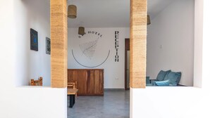 Zona de recepción con un mostrador de madera, un logotipo en la pared y un área de descanso con cojines.