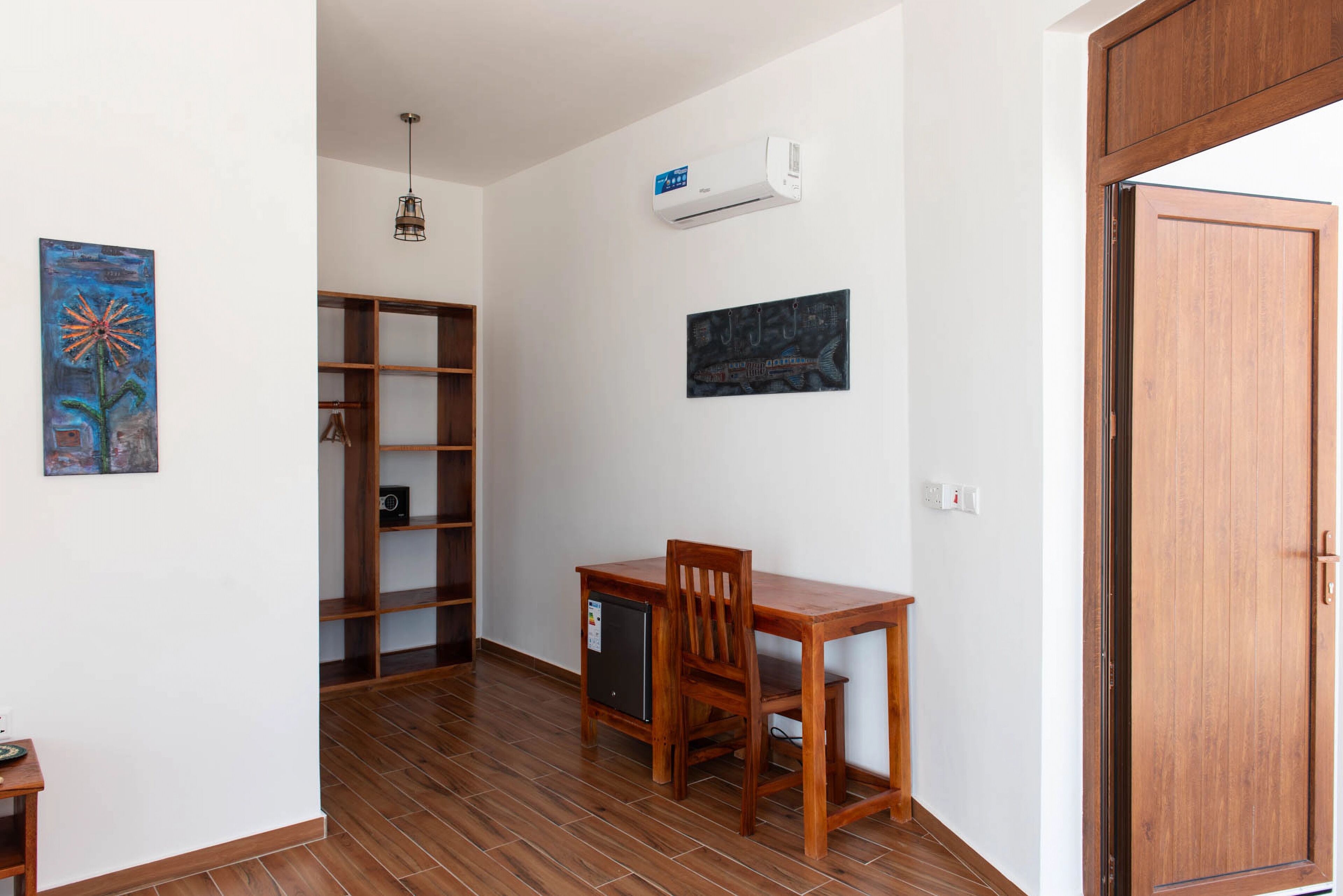 Una habitación con un escritorio de madera, una silla, una estantería y dos obras de arte en la pared.