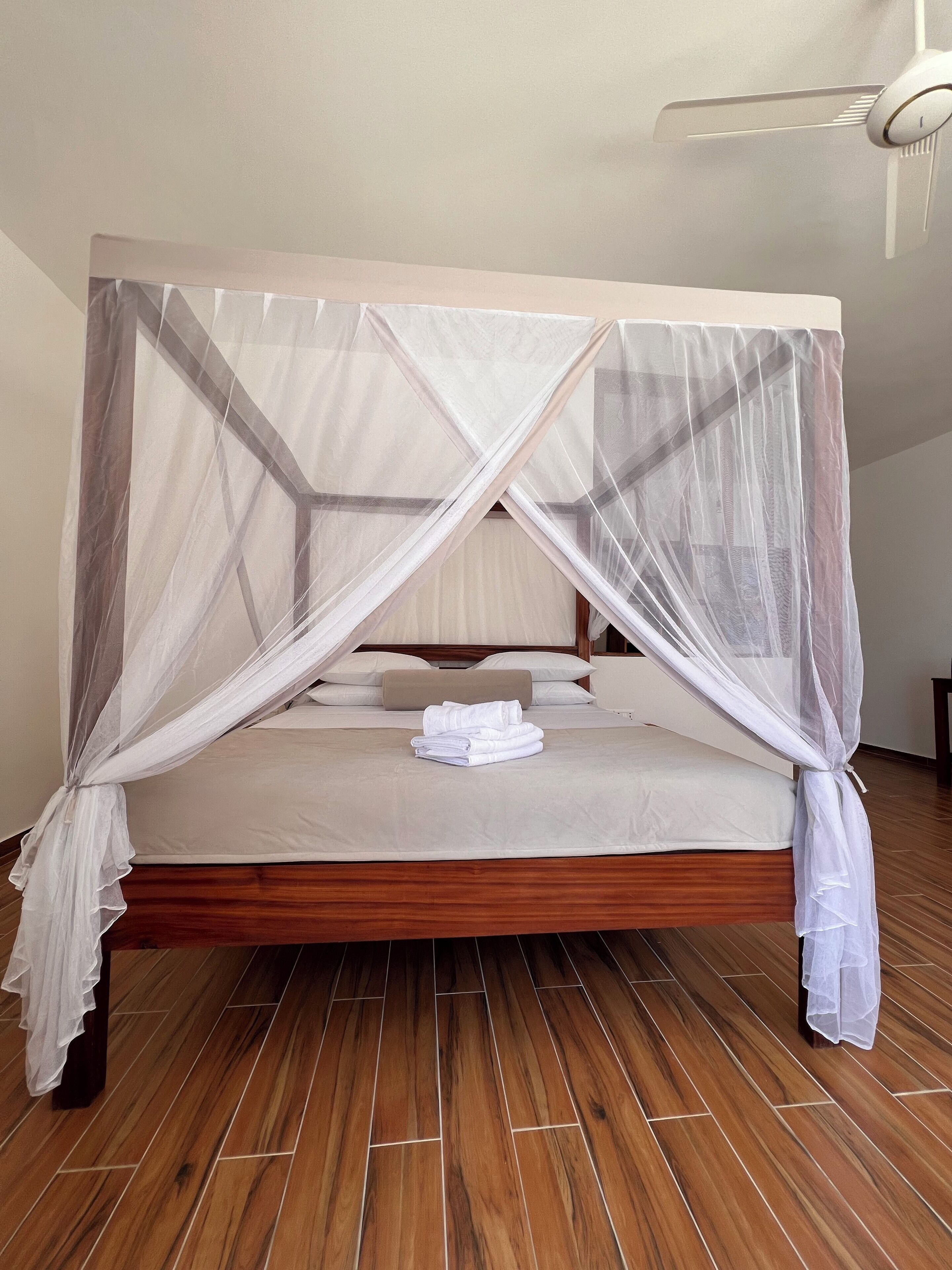 A bed with a canopy, wooden floor, and a ceiling fan.