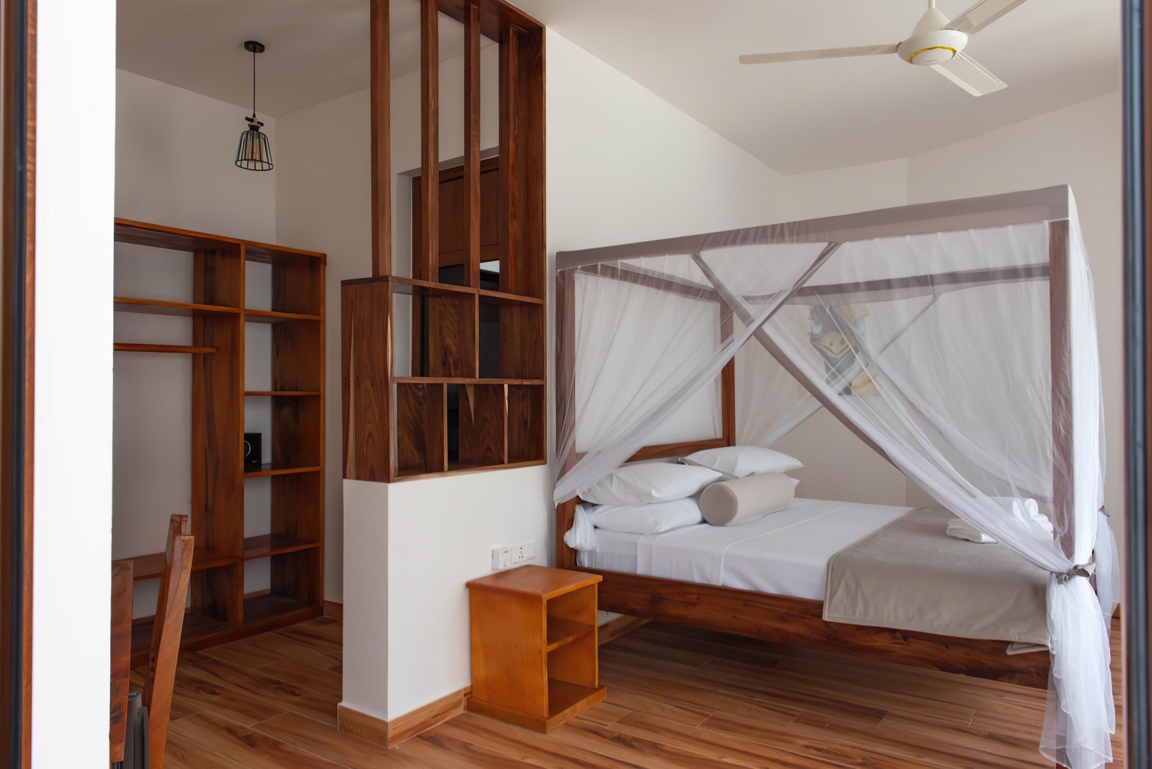 Une chambre avec un lit en bois, un ventilateur de plafond, une table de chevet et des étagères intégrées en bois.