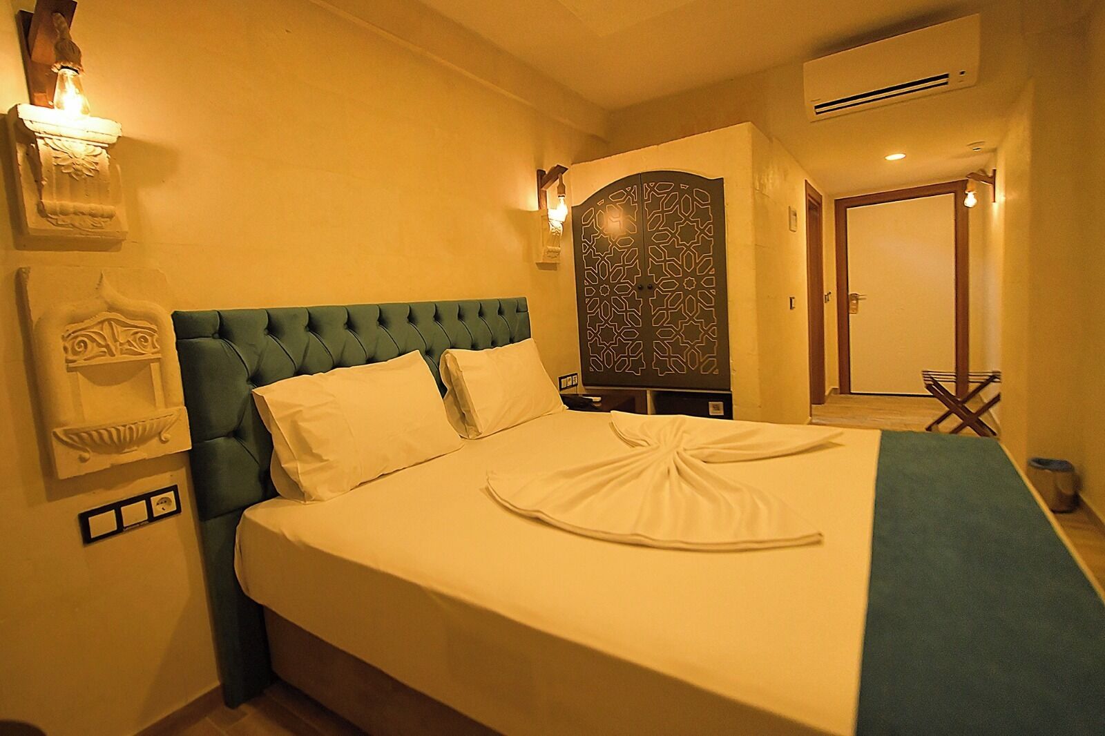A neatly made bed with a green headboard, a decorative wall piece, and a door with a patterned design.