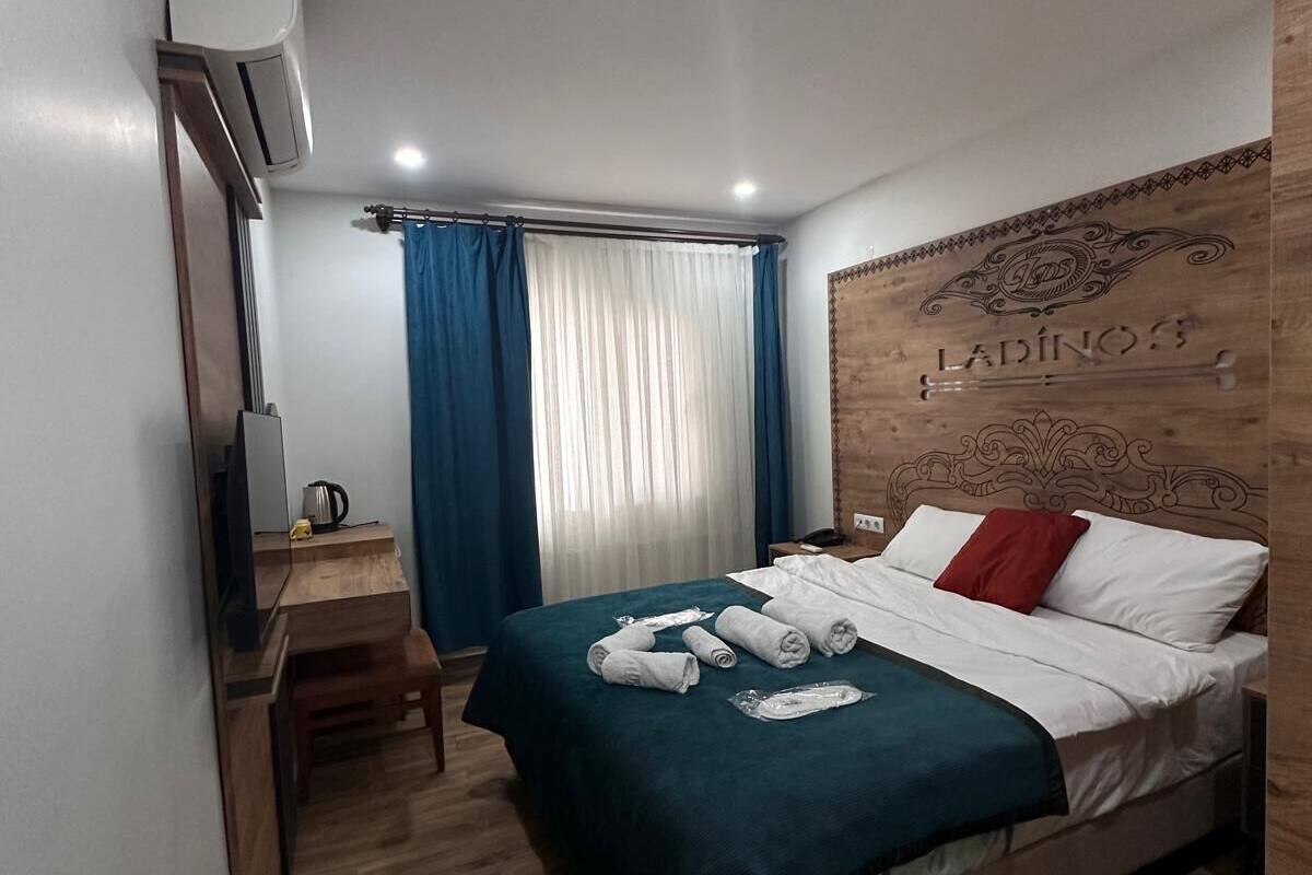 Ett hotellrum med en säng, ett skrivbord, en stol, en tv och ett fönster med gardiner.