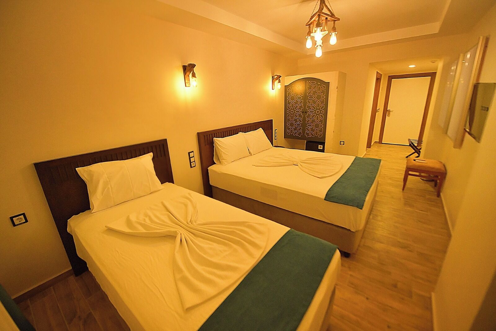 A hotel room with two beds, a wooden floor, a decorative wall panel, and a small stool.
