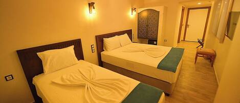 A hotel room with two beds, a wooden floor, a decorative wall panel, and a small stool.