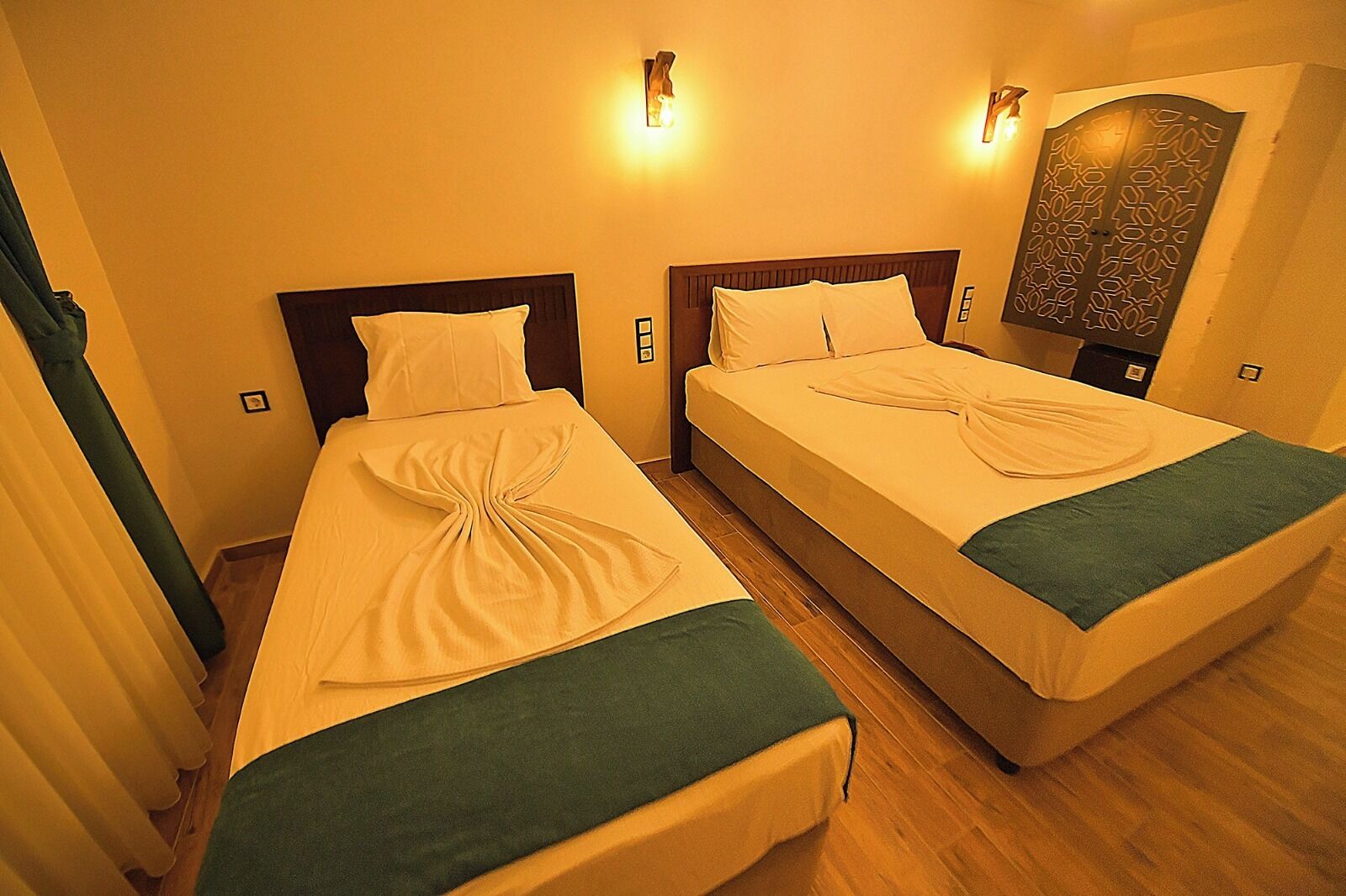 A hotel room with two beds, each with a neatly folded blanket and a green throw at the foot.