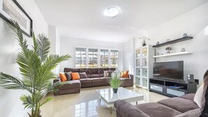 En moderne stue med en hjørnesofa, et fladskærms-tv og en potteplante.