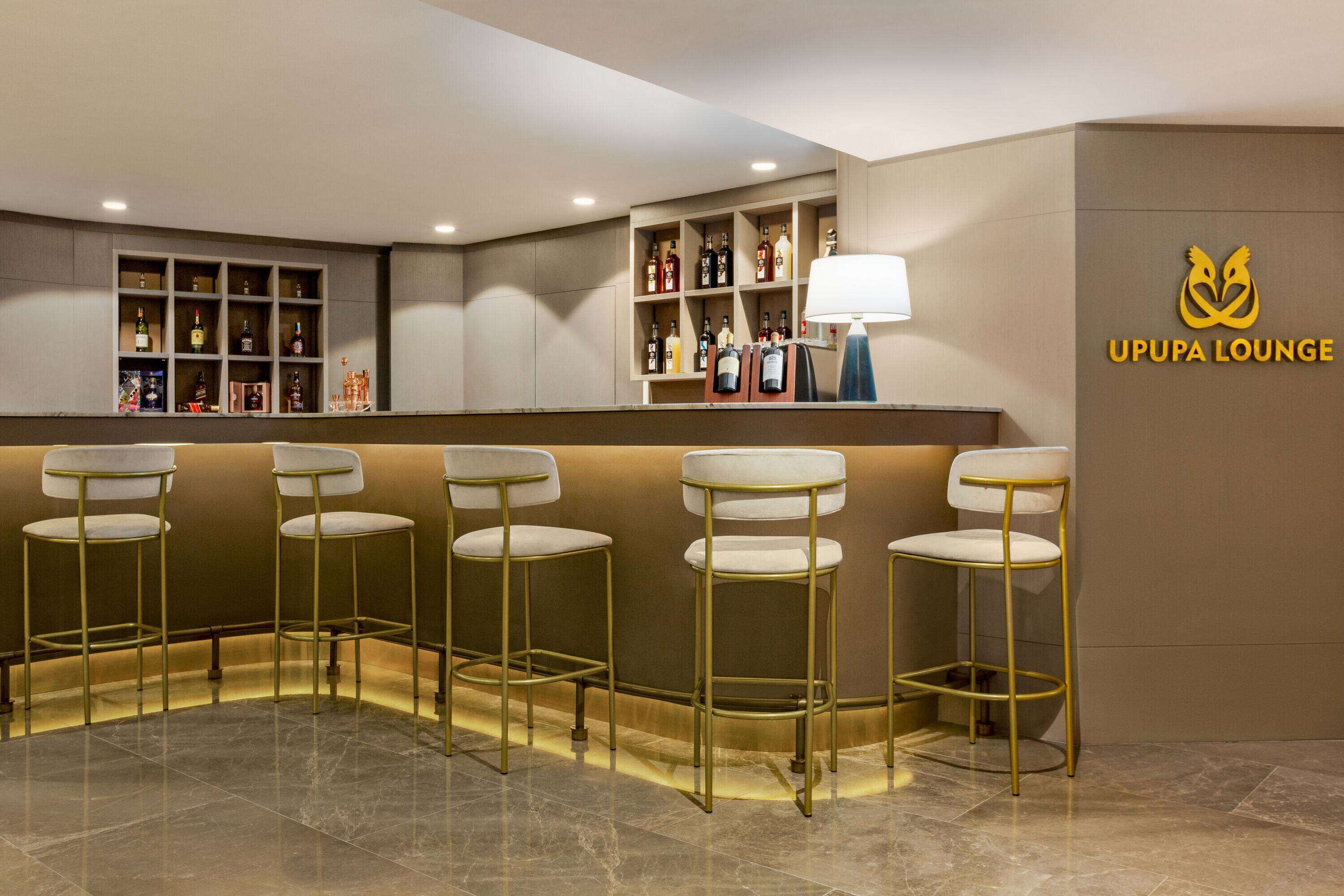 A bar area with a counter, bar stools, shelves with bottles, and a sign reading "UPPA LOUNGE".