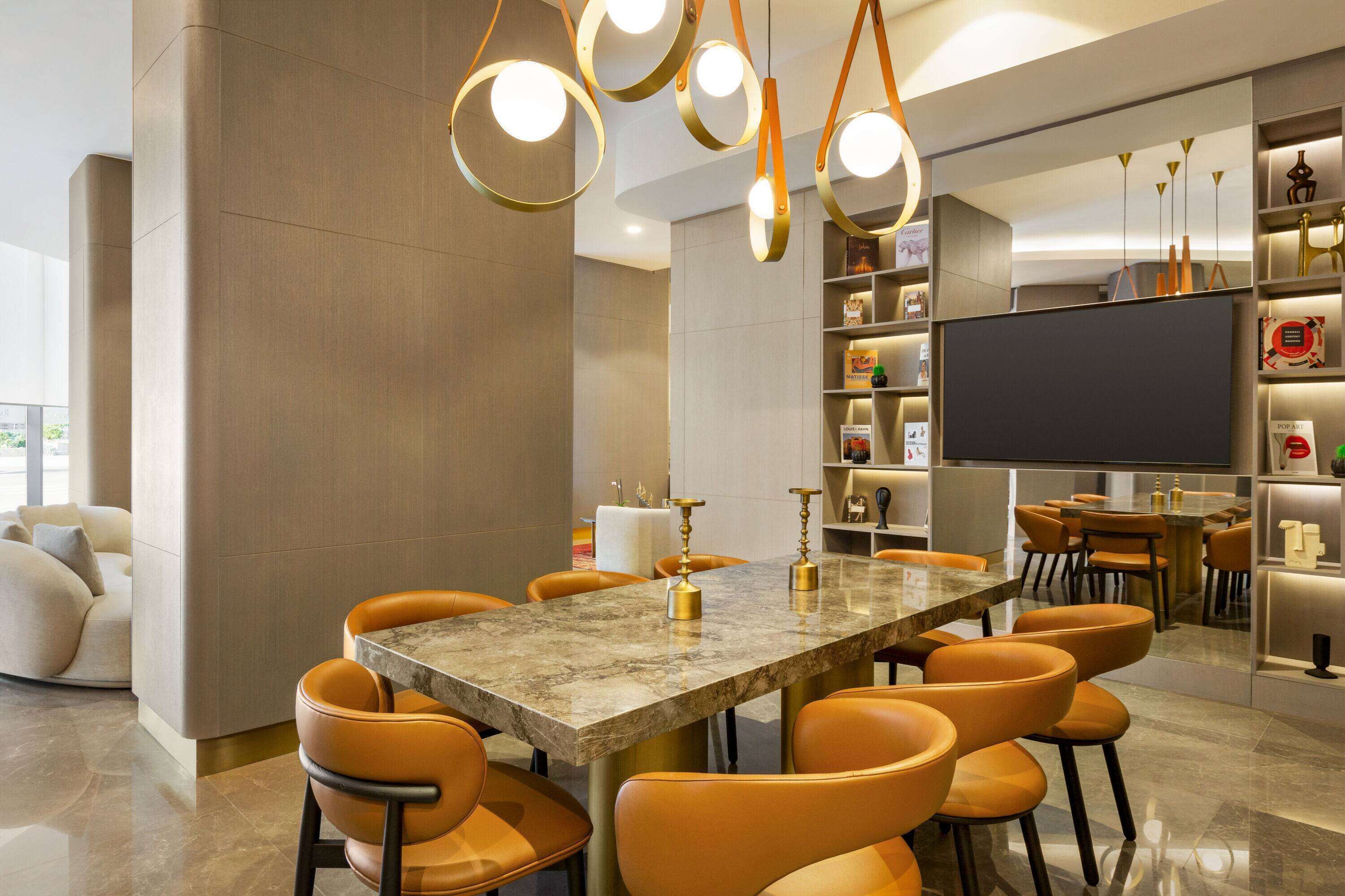 A modern dining area with a marble table, orange chairs, and pendant lighting.