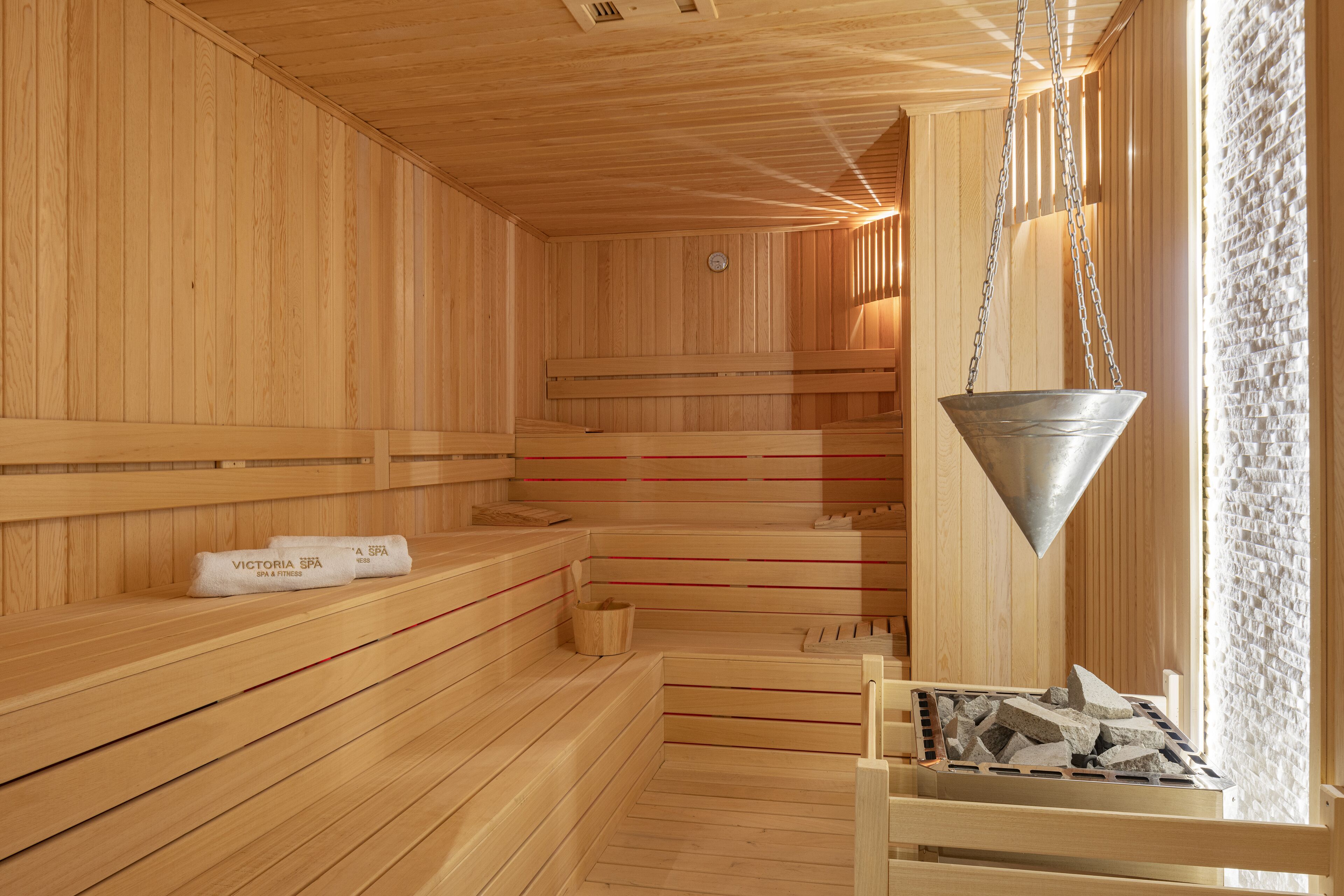 A wooden sauna with benches, a hanging bucket, and a stone tray.