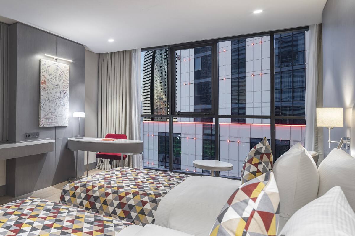 Une chambre d’hôtel moderne dotée d’un grand lit, d’un bureau, d’une télévision et offrant une vue sur le paysage urbain grâce à de grandes fenêtres.