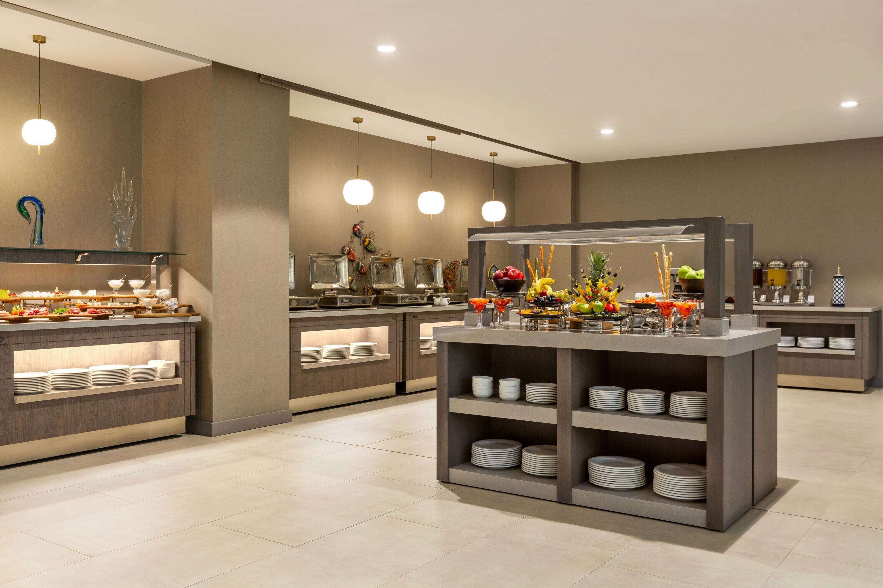 A modern buffet setup with multiple serving stations, each with a variety of dishes and a central display of fruits and flowers.