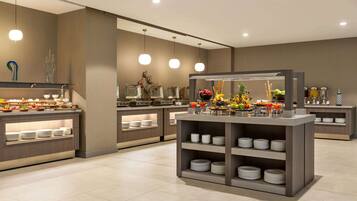 A modern buffet setup with multiple serving stations, each with a variety of dishes and a central display of fruits and flowers.