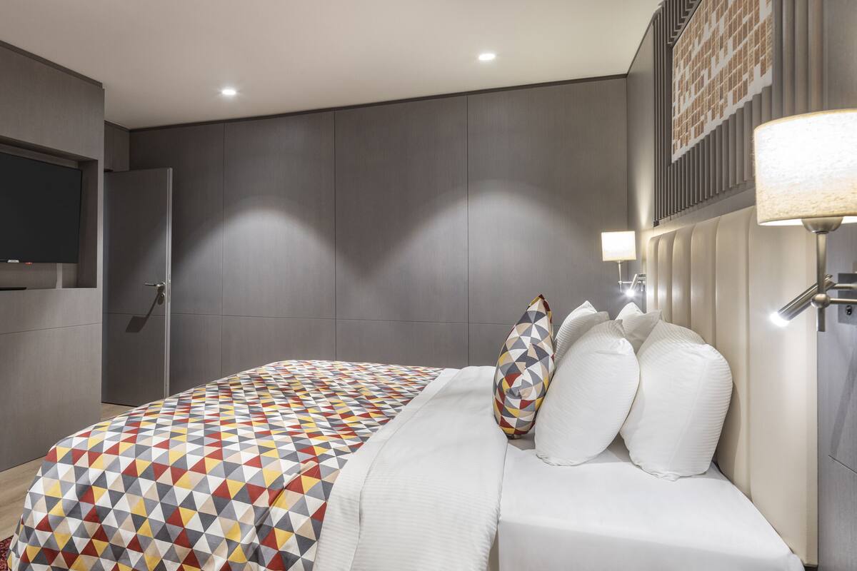 Une chambre moderne avec un grand lit, un téléviseur à écran plat et une lampe fixée au mur.