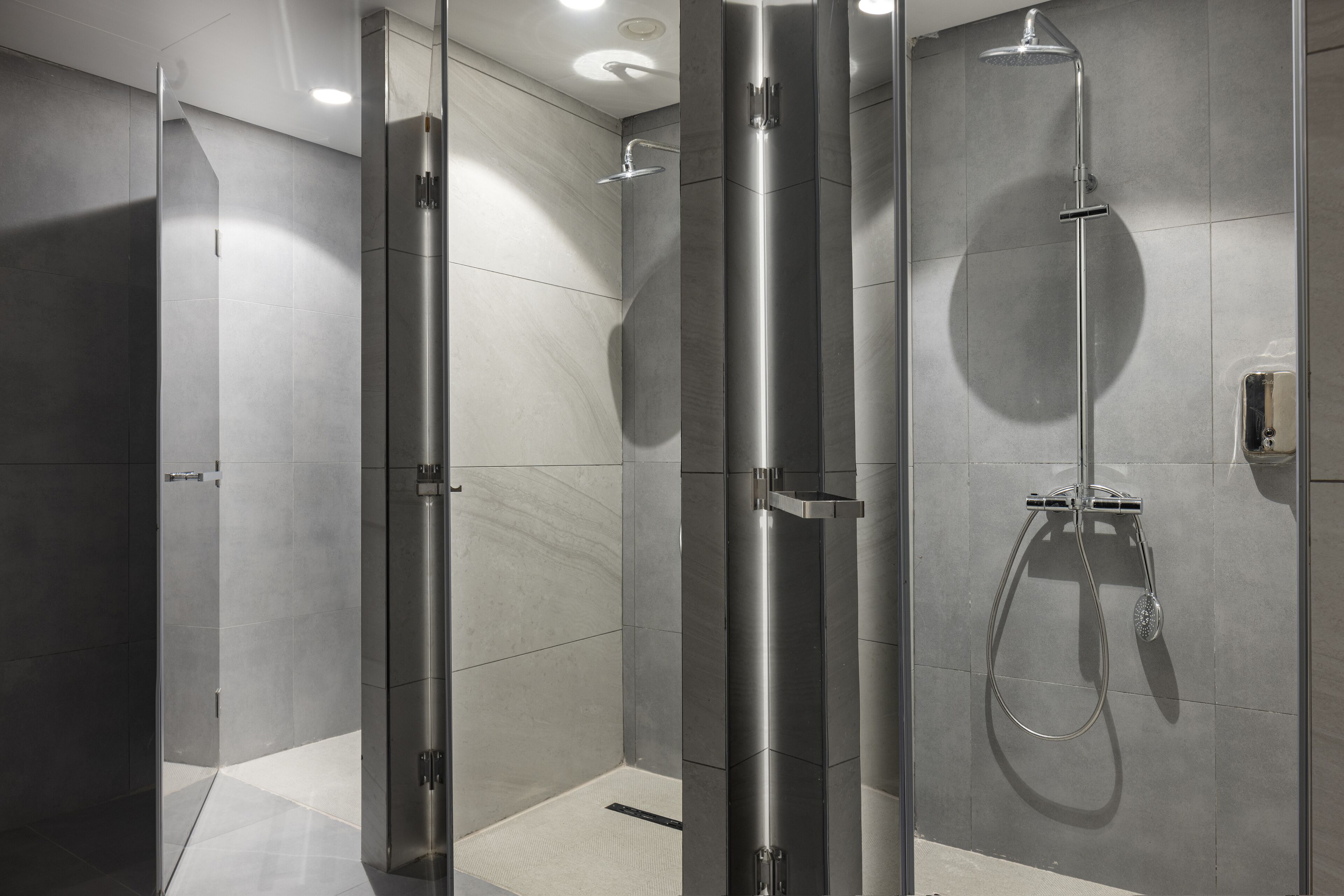 A modern shower area with a glass door, a vertical rain showerhead, and a handheld showerhead.