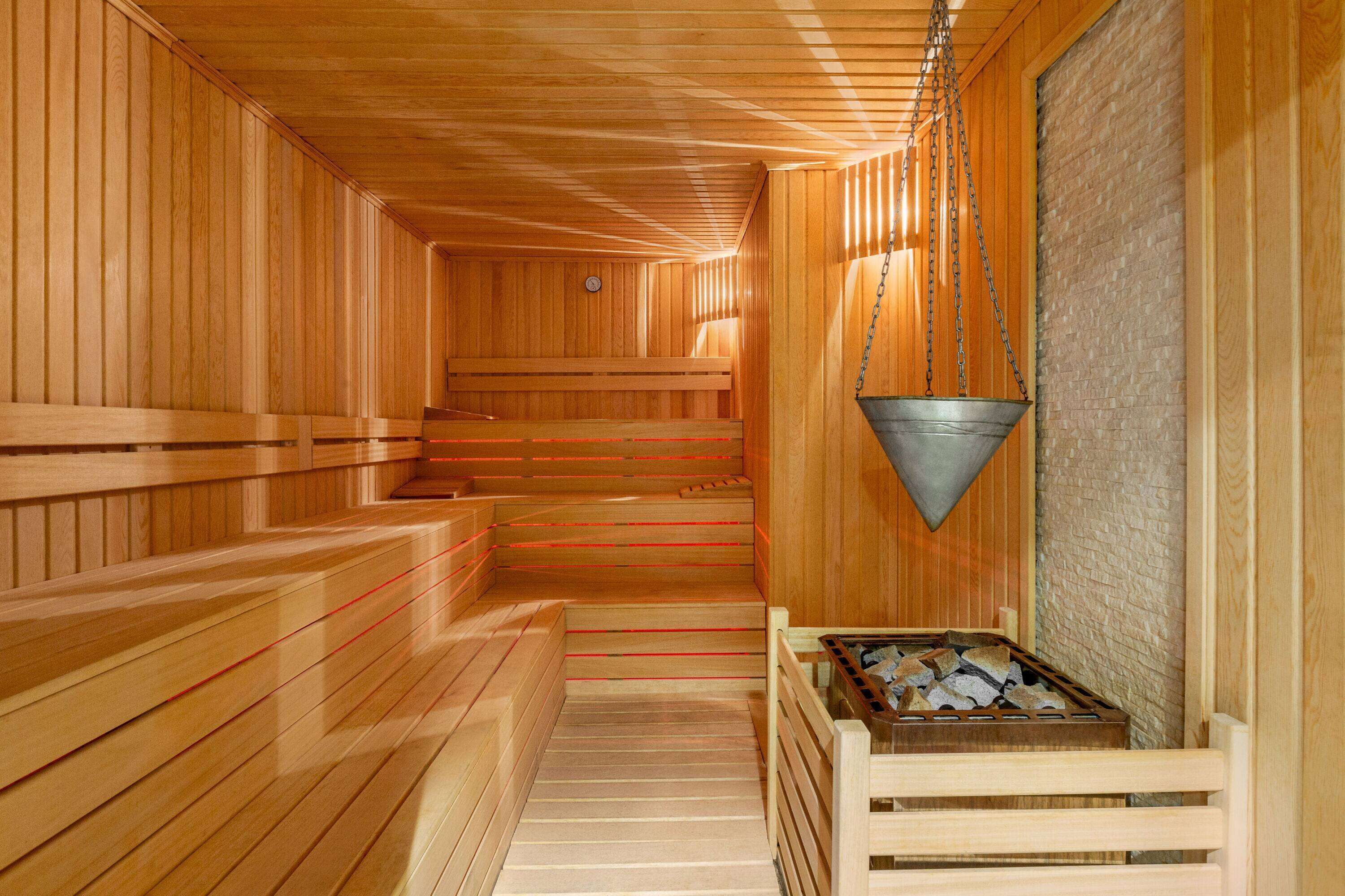 Una sauna de madera con bancos, un cubo colgante y un banco de madera con piedras.