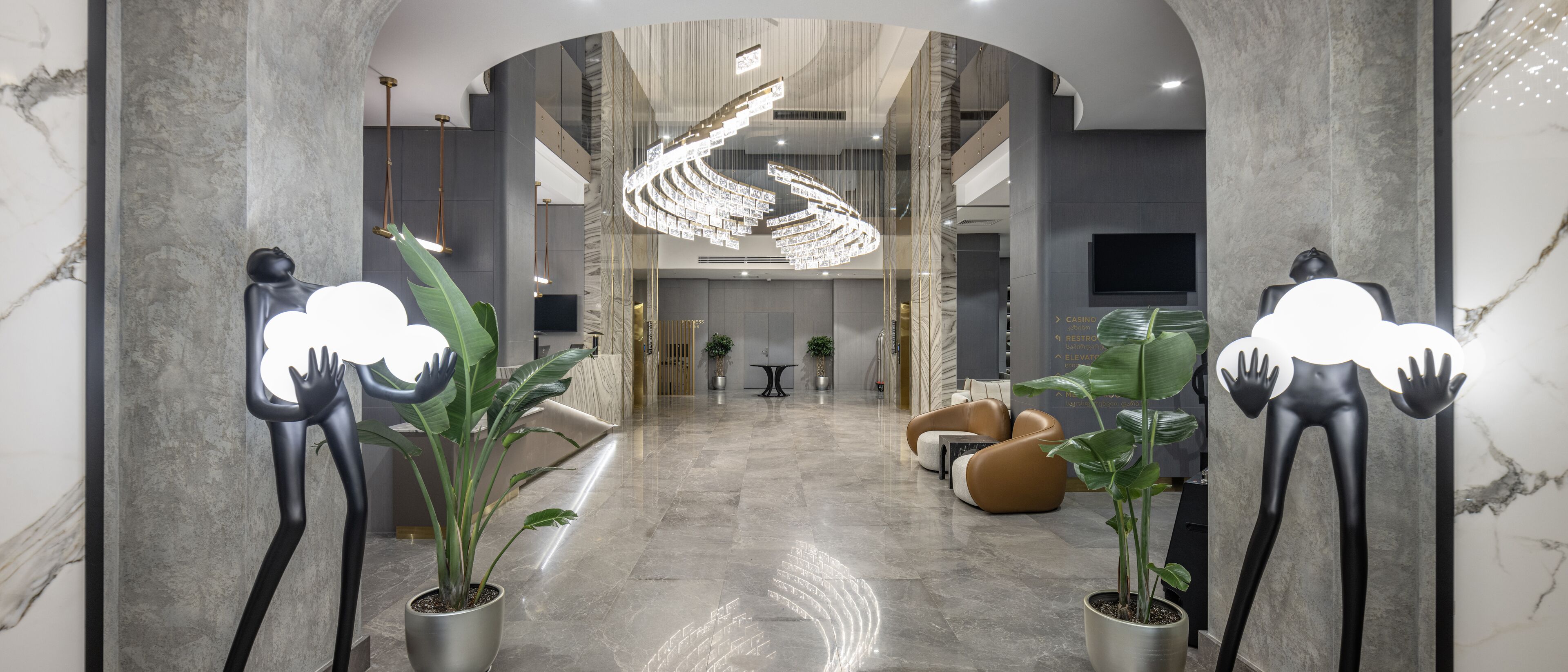 Una hall moderna con pavimento in marmo, un lampadario centrale, piante in vaso e un'area relax.