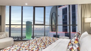 Ein Hotelzimmer mit großem Fenster, einem Bett mit gemusterten Textilien, einer Couch und einem Fernseher.