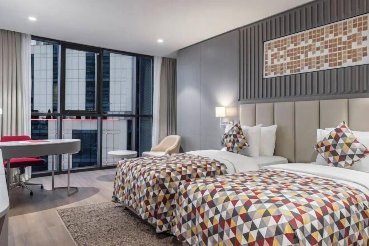 Une chambre d’hôtel avec deux lits, un bureau, une chaise et une grande fenêtre.