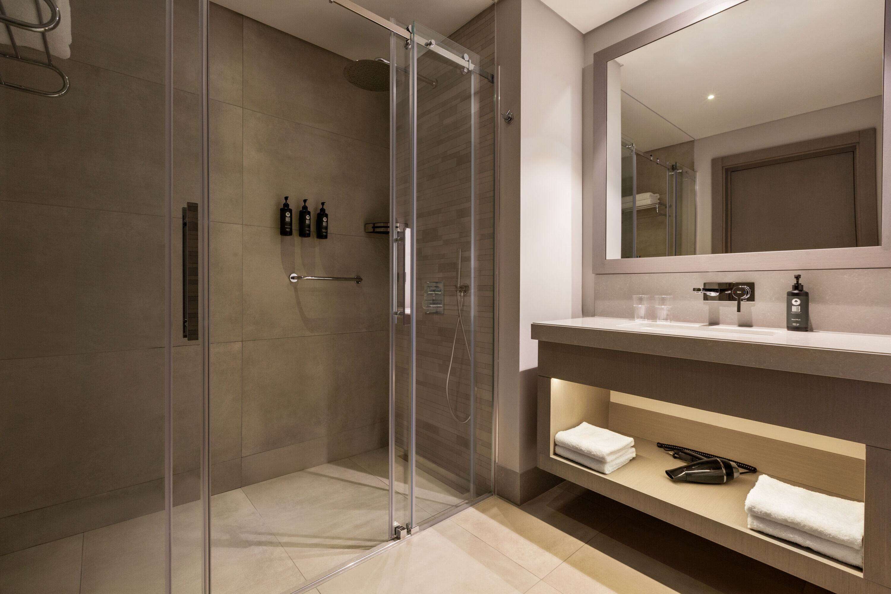 Un bagno moderno con cabina doccia in vetro, uno specchio grande e un mobile lavabo con porta asciugamani e articoli da toilette.